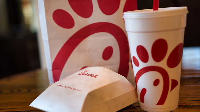 A Chick-fil-A takeout bag, paper fries carton, and fountain drink