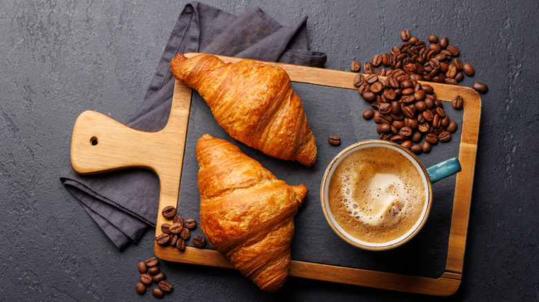 Croissants, beans, and coffee on wooden board; dark background
