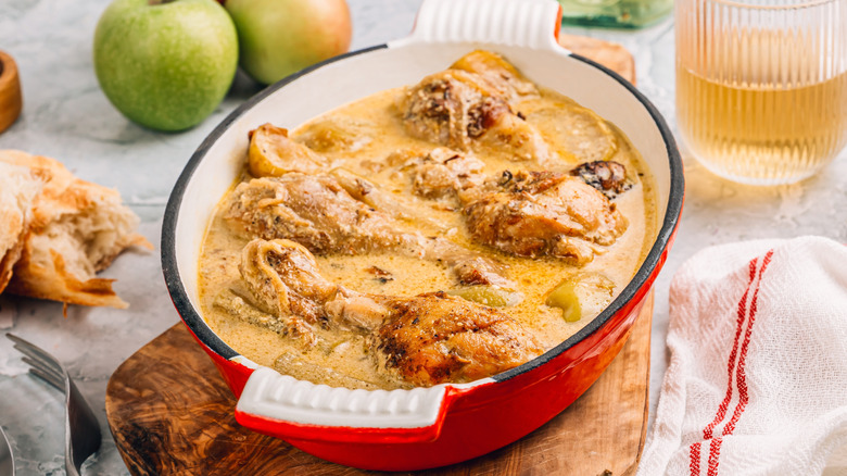 red pan of Poulet au cidre next to apples
