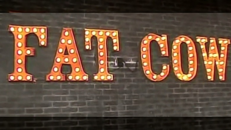 Wall sign that says "Fat Cow" in yellow theater marquee lights