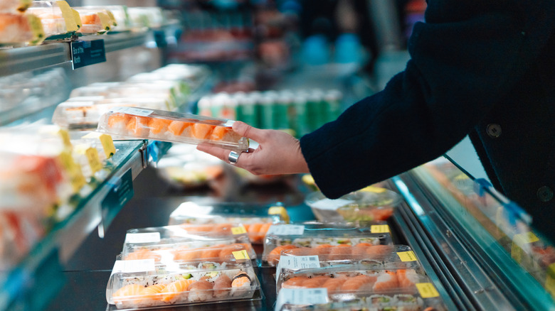 Person picking up box of sushi in grocery store