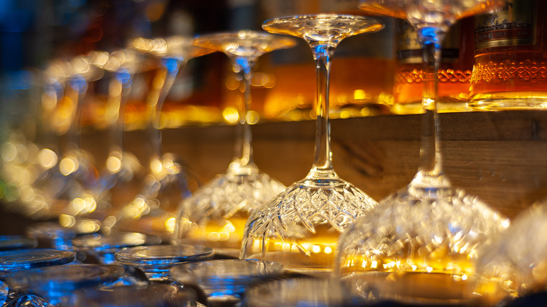 A row of upside-down vintage wine glasses on a bar illuminated by a warm golden light