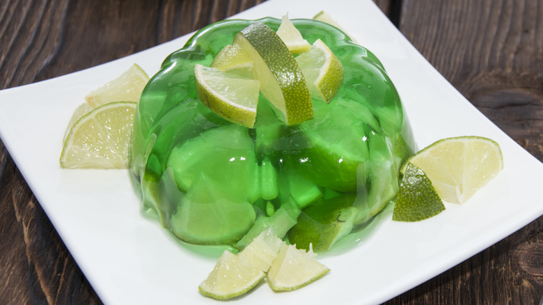 A larger serving of Lime Jell-O on a plate with sliced limes in, on, and beside it.