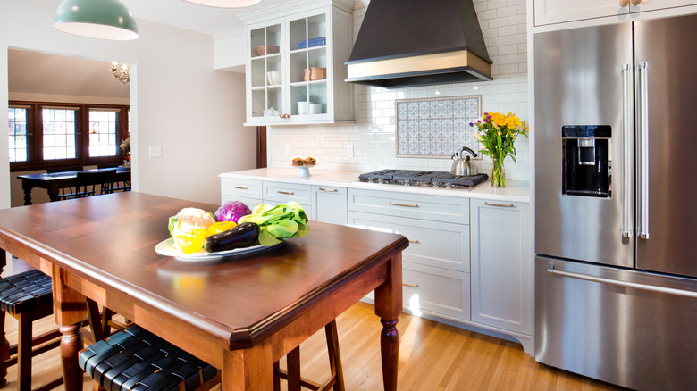 A kitchen with a French door style fridge is cleaned with vegetables on the counter.