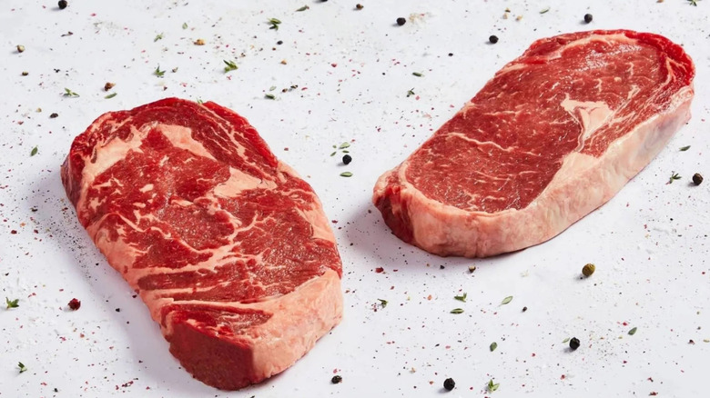 Uncooked ribeye steaks on white surface