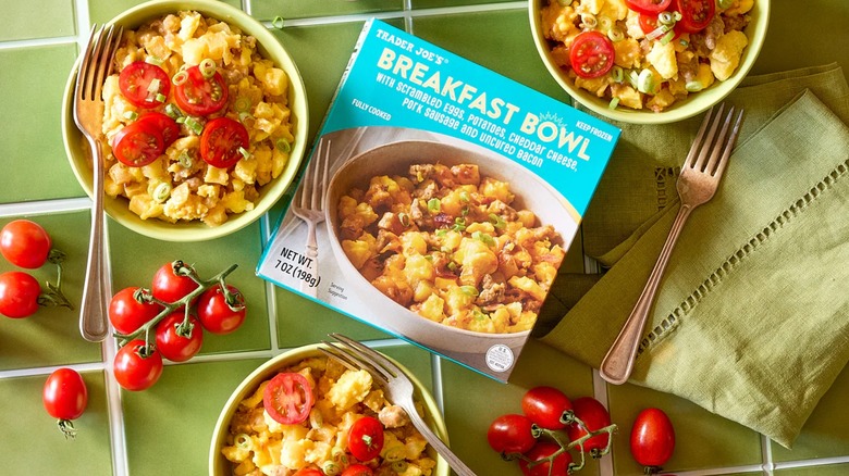 A box of Trader Joe's Breakfast Bowl with 3 green ceramic bowls full of said Breakfast Bowl, plus fresh tomatoes and green onion