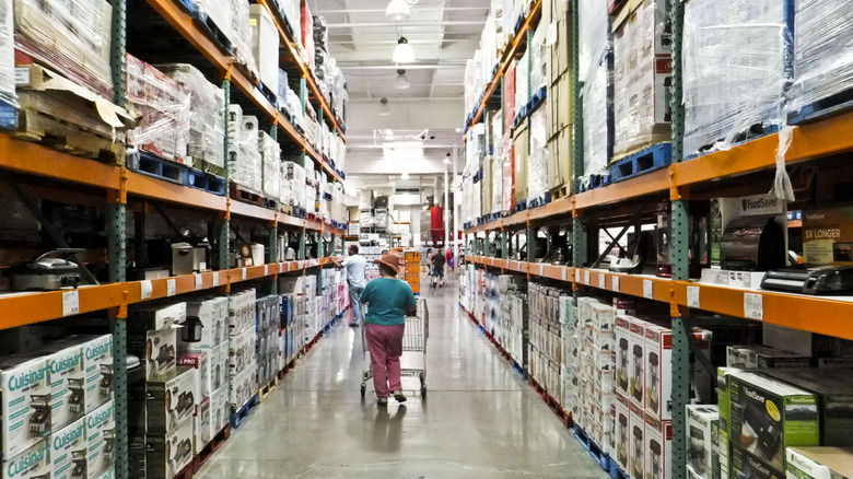 A shopper walks around an aisle of Costco with orange shelves full of appliances.