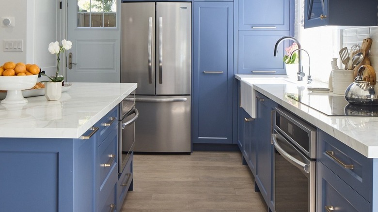 "Love It or List It" kitchen with blue cabinetry and island, white marbled countertops, and white walls.