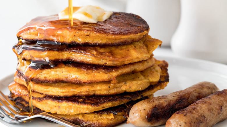 Stack of sweet potato pancakes with maple syrup and sausages