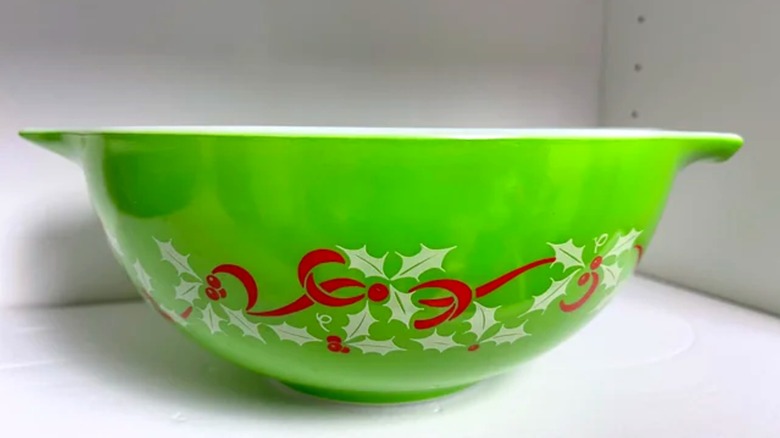 A bright green holiday Pyrex bowl with red ribbon and white holly leaves