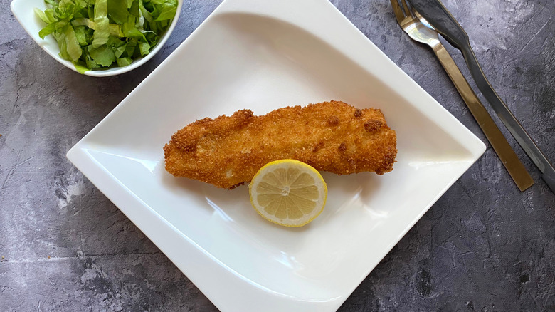 Fried breaded fish on a plate with half of a lemon