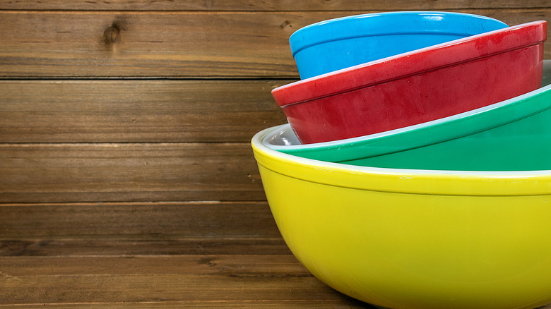 Stacked red, red, green, and yellow Pyrex bowls with a wood background