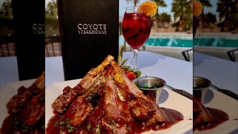 Coyote Steakhouse's New Zealand rack of lamb with a glass of sangria and restaurant menu on a poolside table