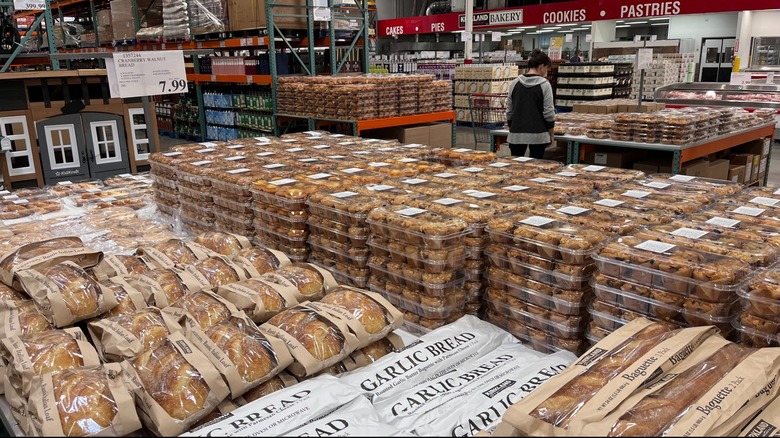 Costco's bakery department with plastic packages of food and a single shopper perusing.