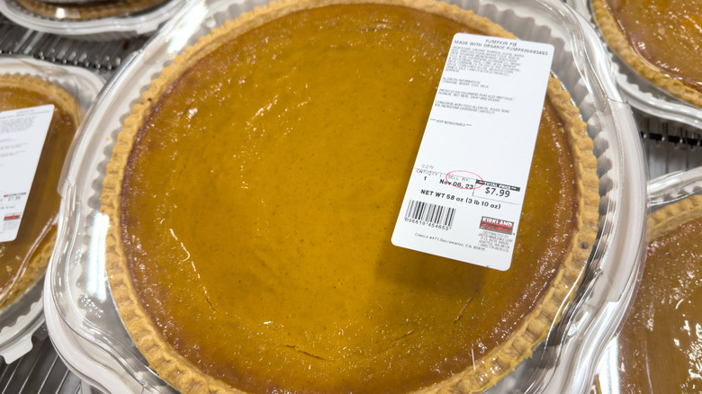 Pumpkin pie in a tin with a plastic lid and label with other pumpkin pies