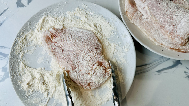 floured chicken breast on a white plate