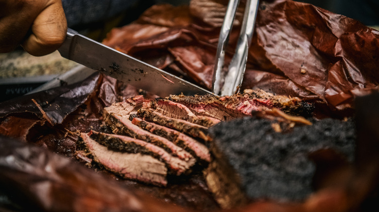 a close-up of hands cutting smoked brisket