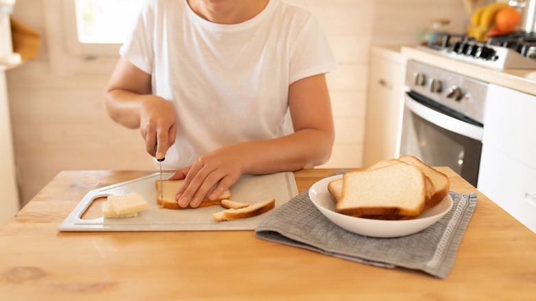 person cutting of bread crust on a cutting board while sitting at a table