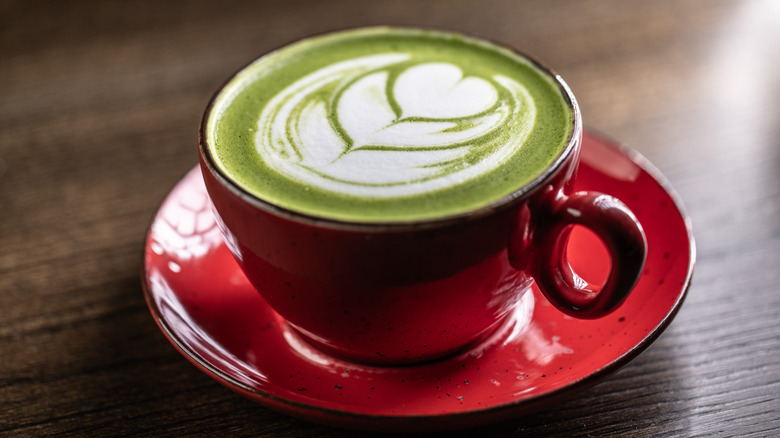 Matcha latte with a heart design in a red cup on a table