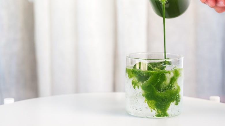 Pouring matcha into a glass filled with tonic and ice