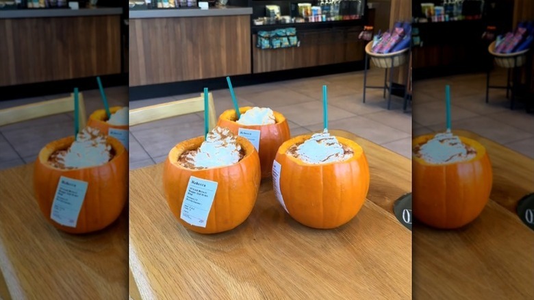 Three Starbucks drinks in carved pumpkins on table
