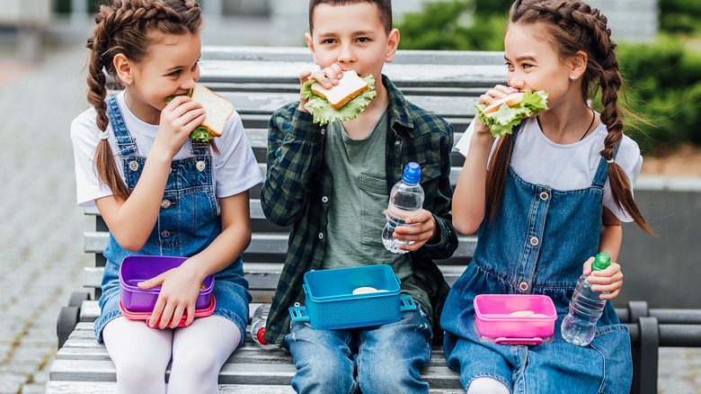 three kids eating from lunchboxes