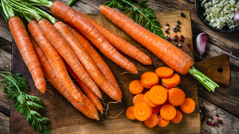 Raw carrots, some of them sliced, on a wooden cutting board