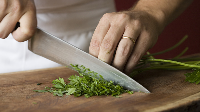 Knife cutting herbs on board