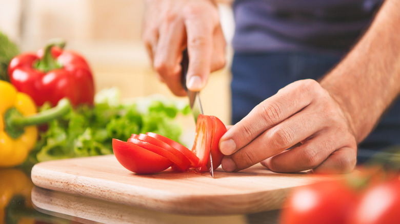 Man slicing a fresh red tomato on a wooden cutting board
