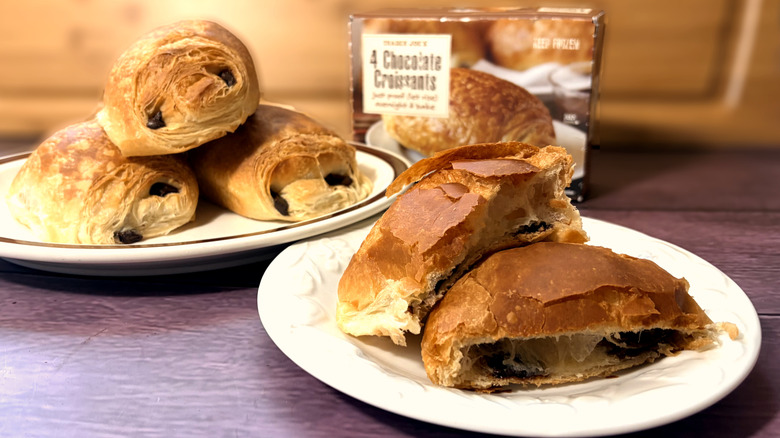 package and plate of three chocolate croissants behind one sliced chocolate croissant on front plate