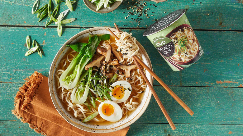 a bowl of ramen with mushrooms, bok choy, soft-boiled egg, and furikake, with a cup of Trader Joe's miso ramen soup next to the bowl
