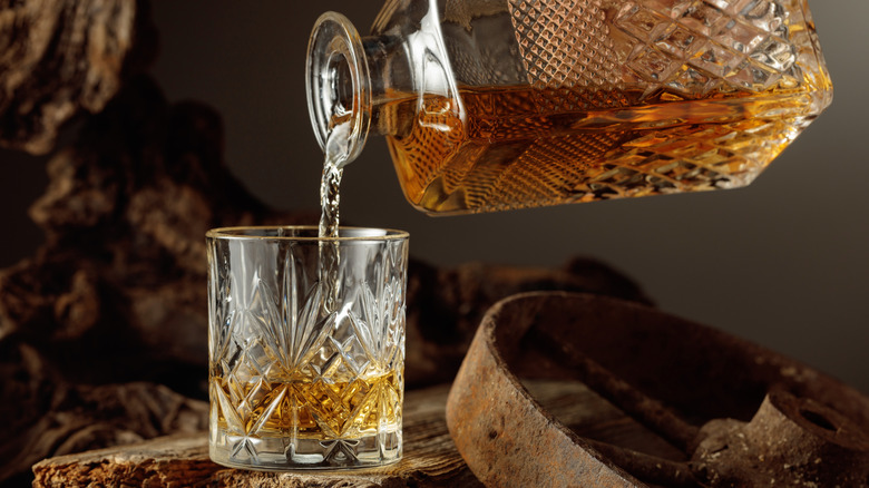Whiskey being poured from a decanter into a rocks glass