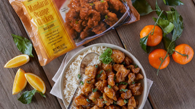 A package of Trader Joe's Mandarin Orange Chicken necxt to a bold of chicken, rice and oranges