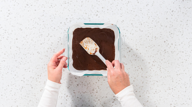 Hands spread chocolate into lined square pan with spatula