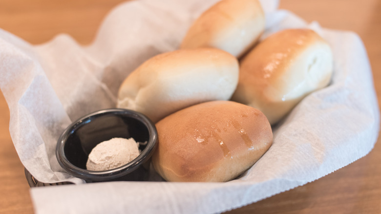 Texas Roadhouse rolls in basket lined with paper and a black ramekin of butter.