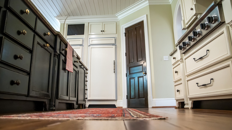 Low angle image of kitchen with thin rug on wood floor.
