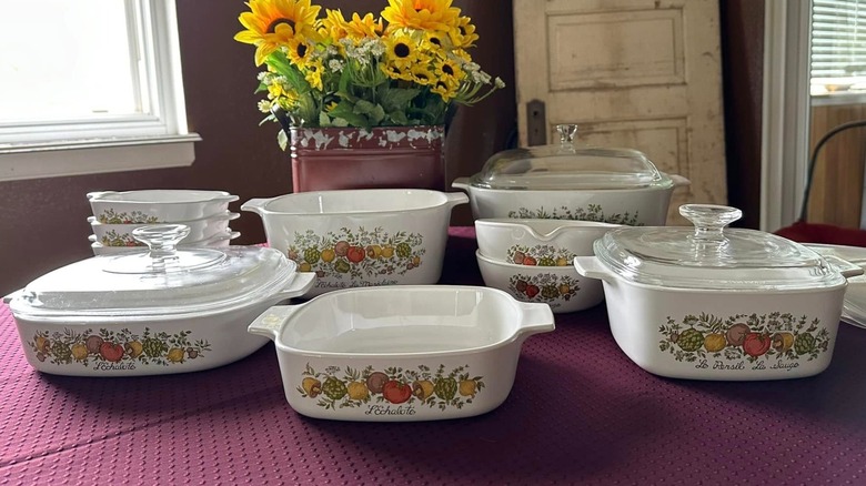 Retro set of "Spice O' Life" CorningWare on a maroon tablecloth with a tin of sunflowers