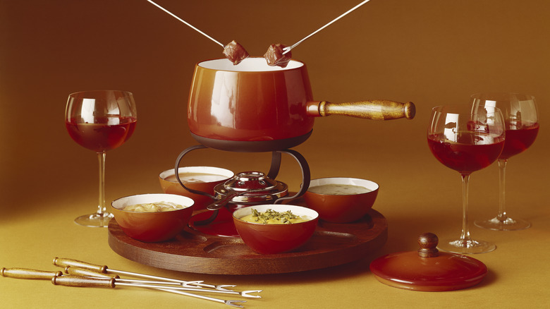 Retro fondue set on a lazy Susan with glasses of red wine