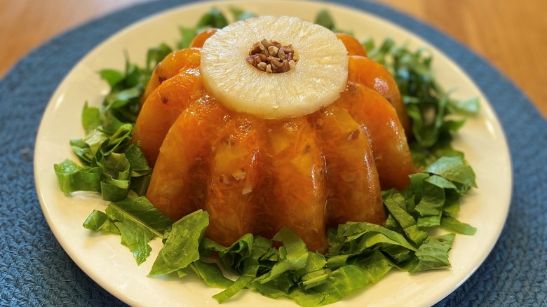 Molded gelatin on a bed of lettuce with a pineapple ring on top and chopped nuts in the center