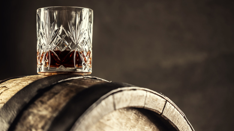 A glass of whiskey balances on an aging barrel