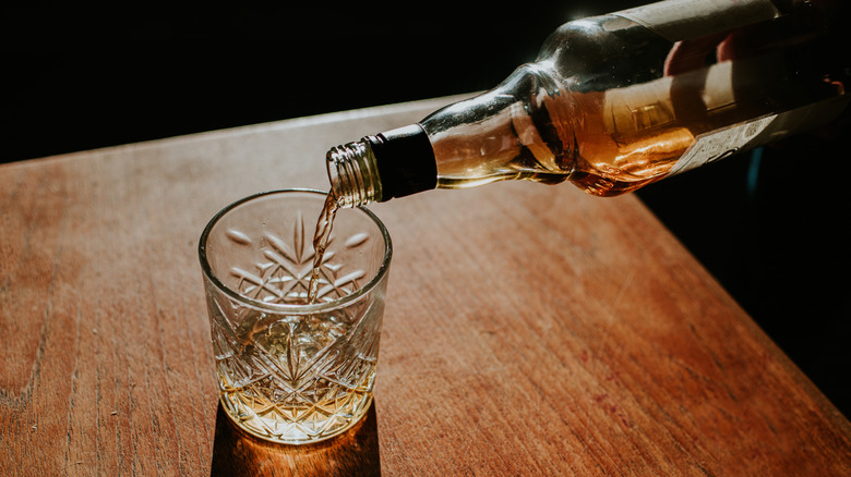 A bottle of whiskey is poured into a tumbler