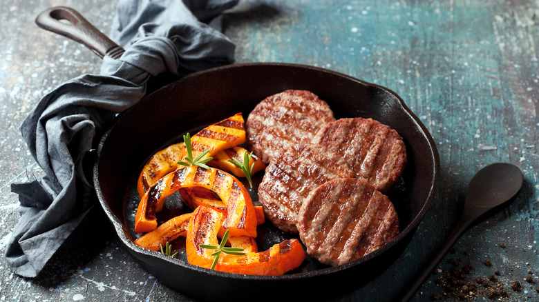 Burgers in cast iron grill pan with vegetables