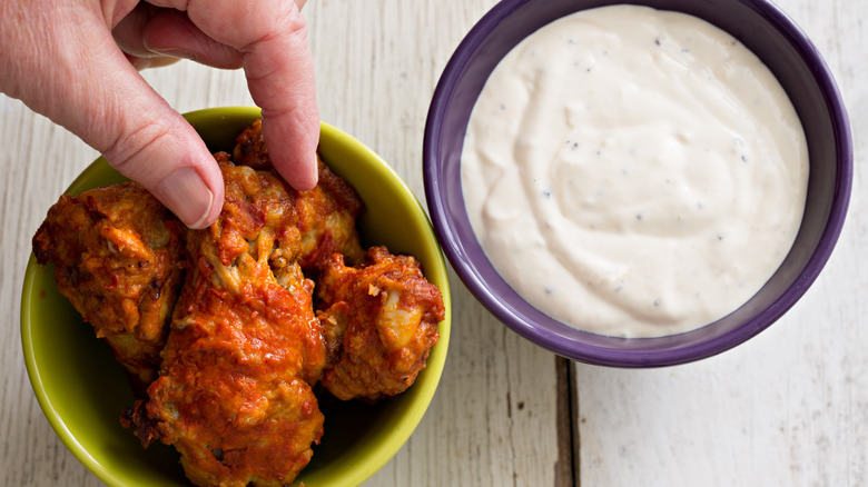 A hand reaches for buffalo wings next to blue cheese dip