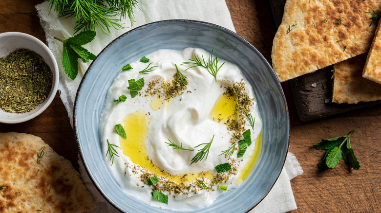 herby dip in a bowl surrounded by fresh herbs and pita crisps