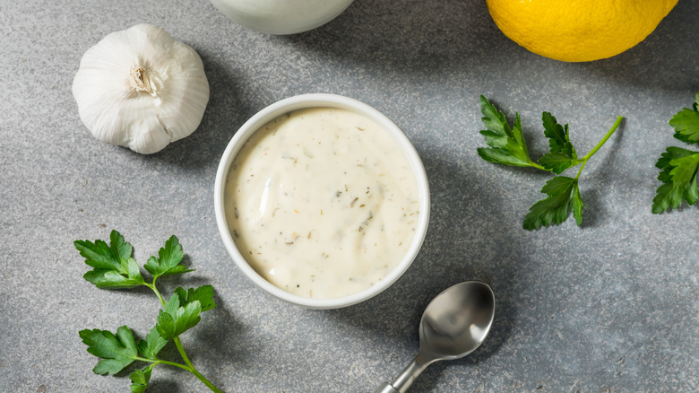 ranch dip in a bowl with a spoon with parsley, garlic and a lemon around it