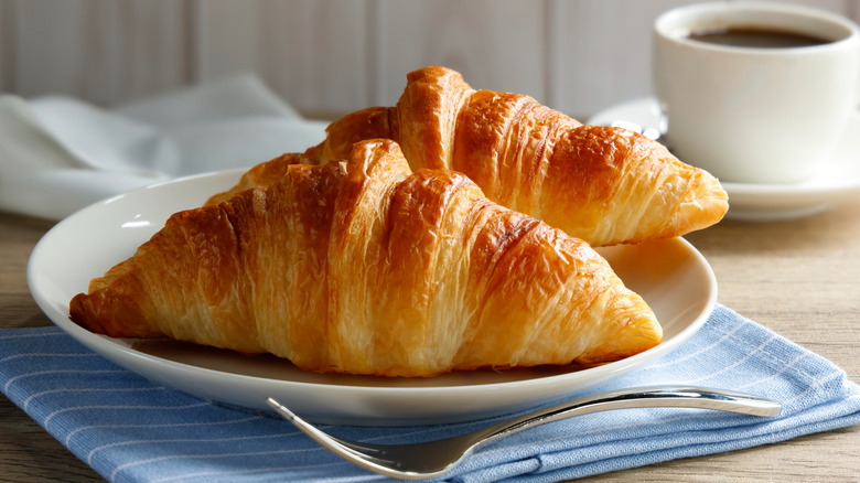 Two golden croissants on a plate with a black coffee