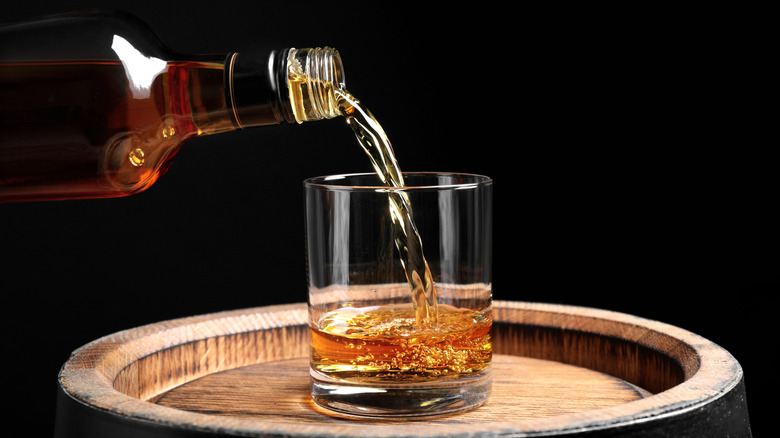Whisky poured from bottle to glass on a barrel