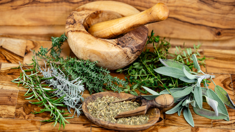 Severall fresh herbs gathered together on a wooden surface next to a pestle