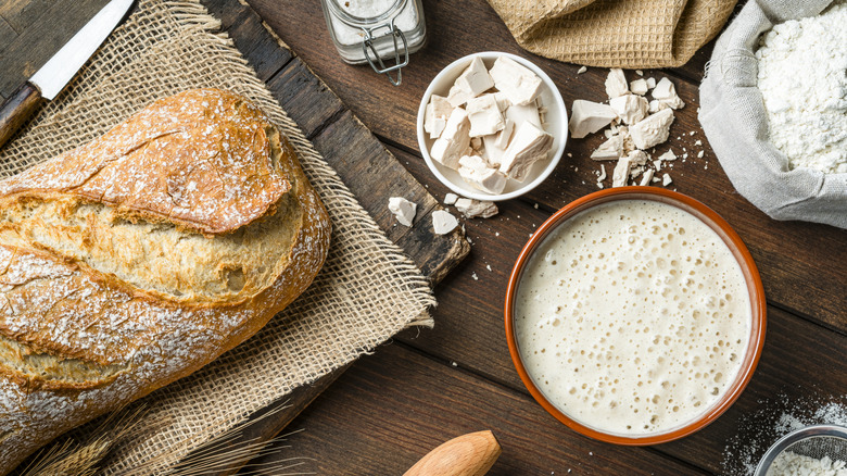 An overhead view of a fresh loaf of bread, with ingredients and utensils dotted around it