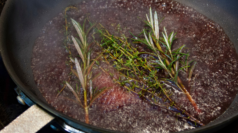 A pan deglazes with rosemary, thyme, and red wine